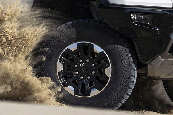 Folsom Buick GMC FOLSOM - Close-up of GMC Hummer EV black alloy wheel and all-terrain tire with sand flying in motion