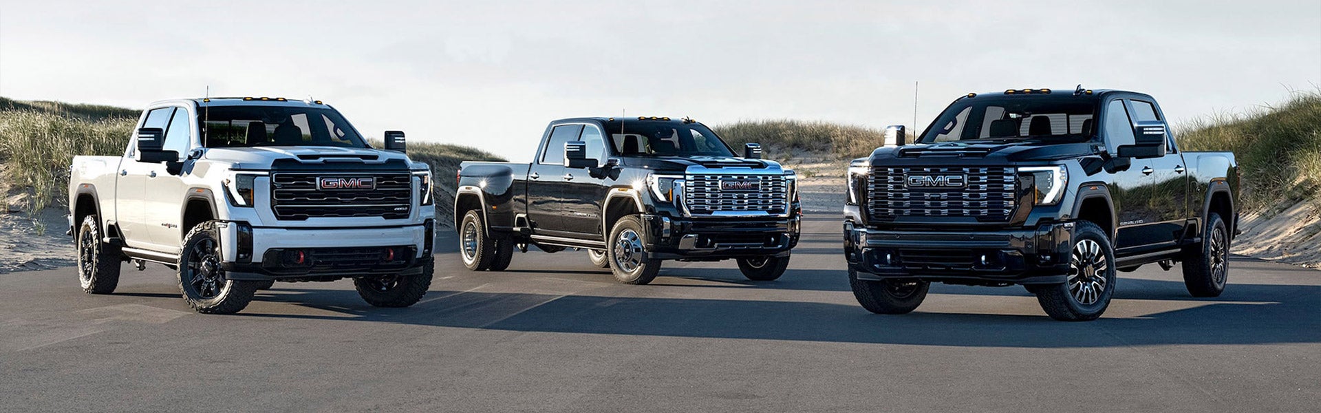 Folsom Buick GMC FOLSOM CA - 2025 GMC Sierra 2500HD lineup showcasing three trim levels with distinctive grilles and wheel designs on coastal terrain